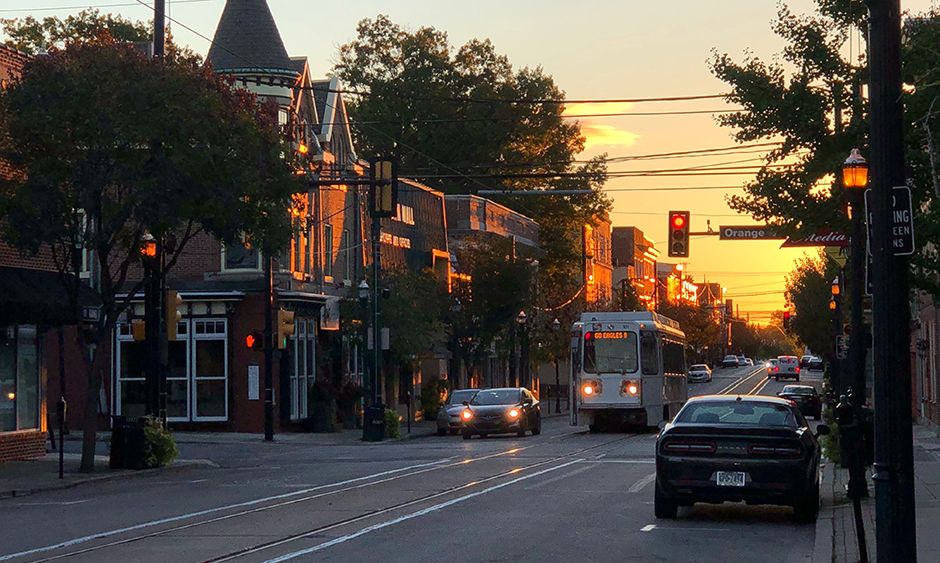 A trolley travels along a road with the sun rising behind it