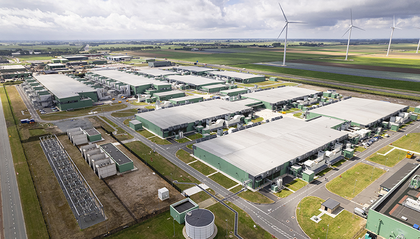 An aerial view of a data center with wind turbines in the background