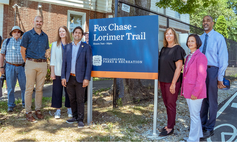 Representatives from various agencies stand around the new sign marking the Fox Chase Lorimer Trail