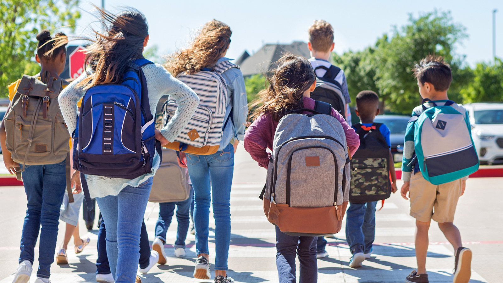 Children with backpacks walk through a crosswalk