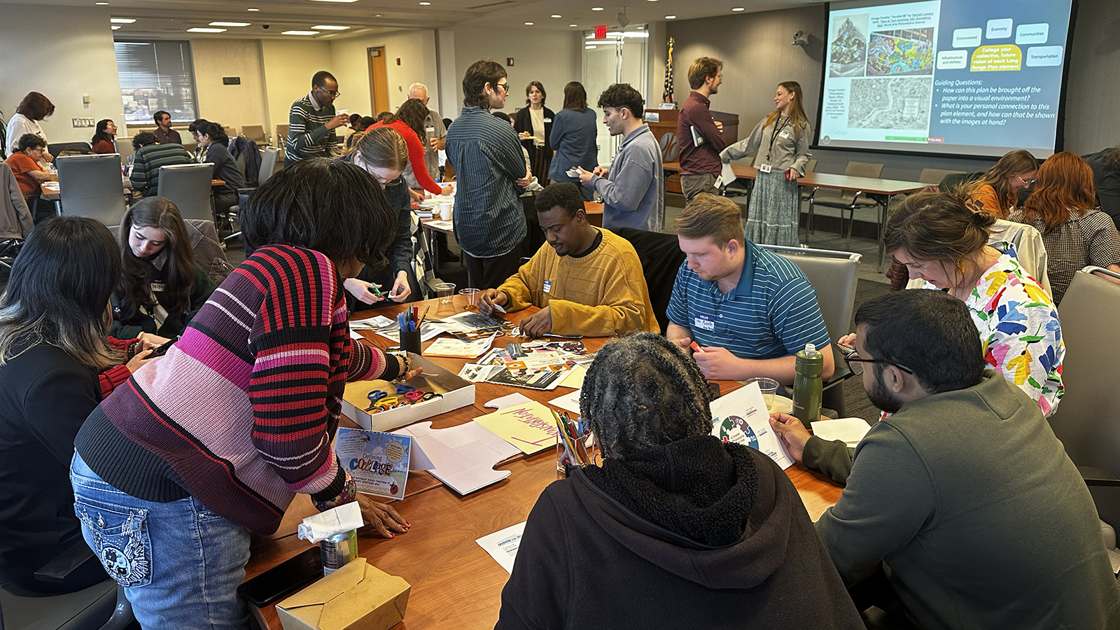 People gathered around a table where they are working on a group collage in a busy meeting room