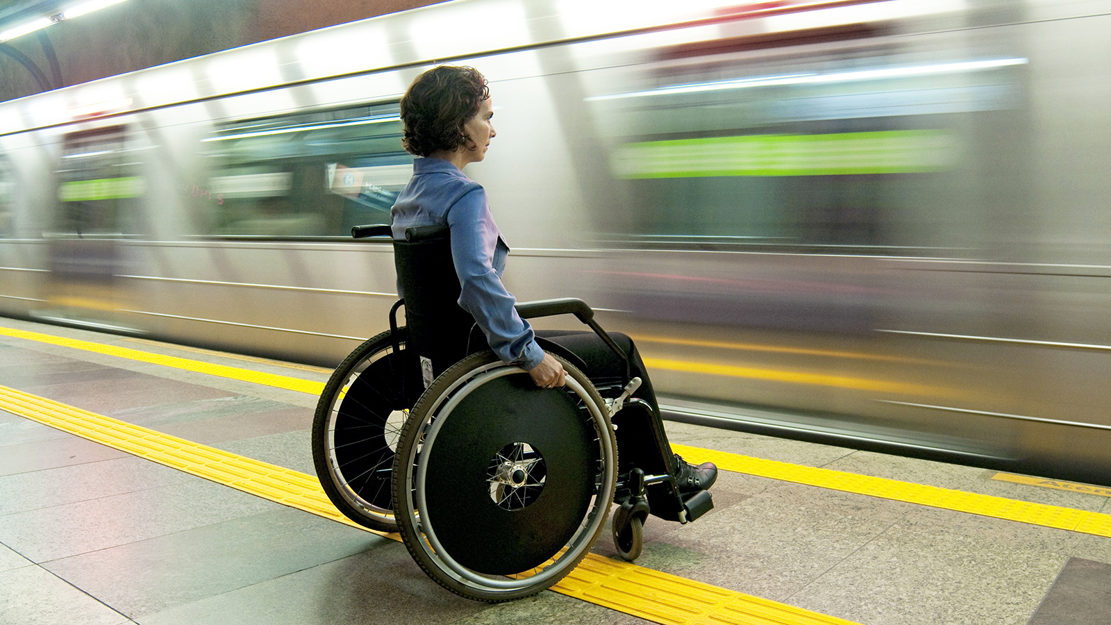 A person in a wheelchair waits on a platform as a subway pulls into a station