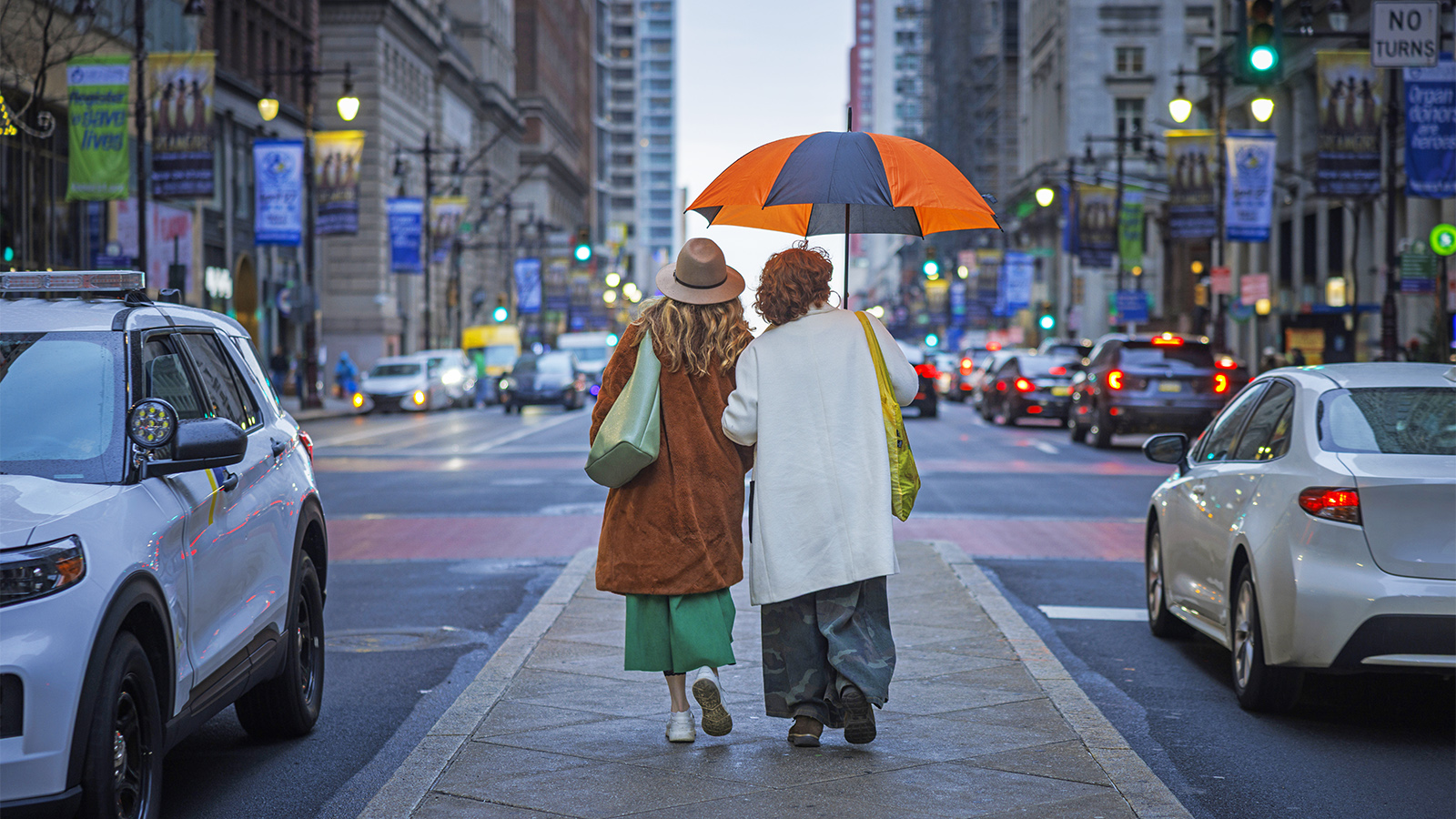 Two women sharing an umbrella walk on a pedestrian median in Center City Philadelphia.