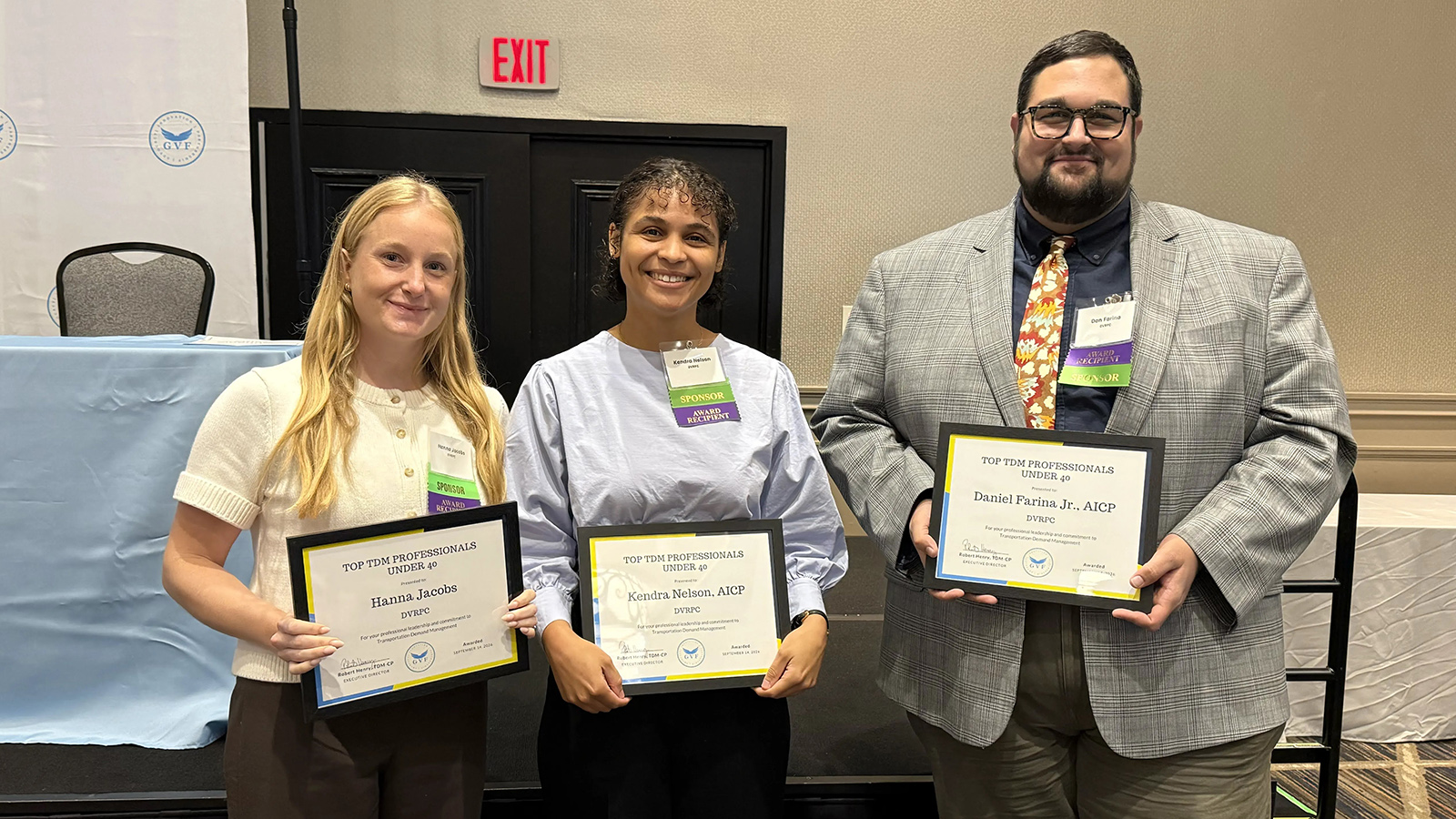 Three people stand together holding award certificates