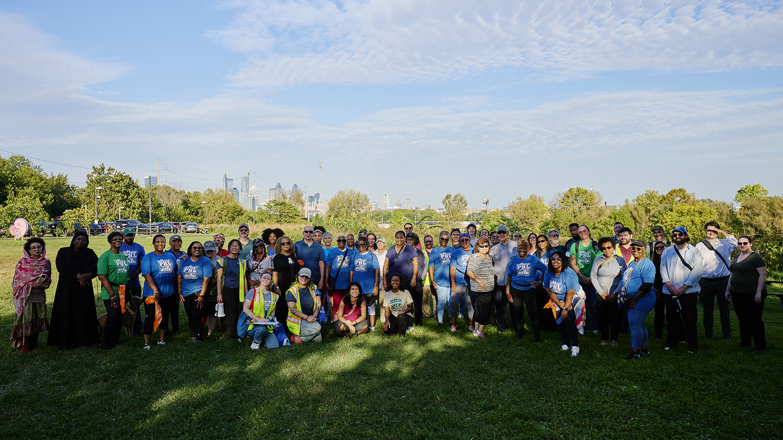 Approximately 50 people stand together in a park for a photo