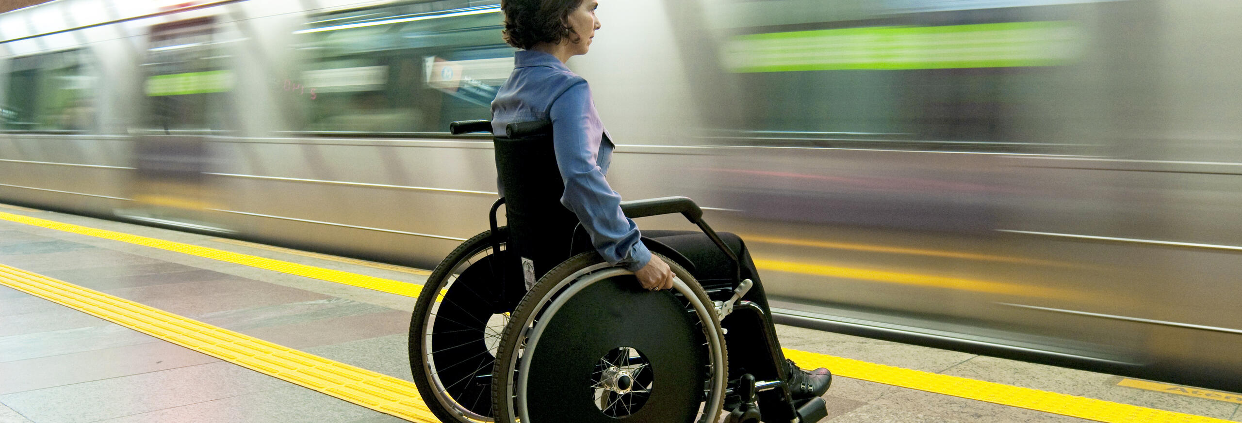 A person in a wheelchair waits on a subway platform as a train pulls in